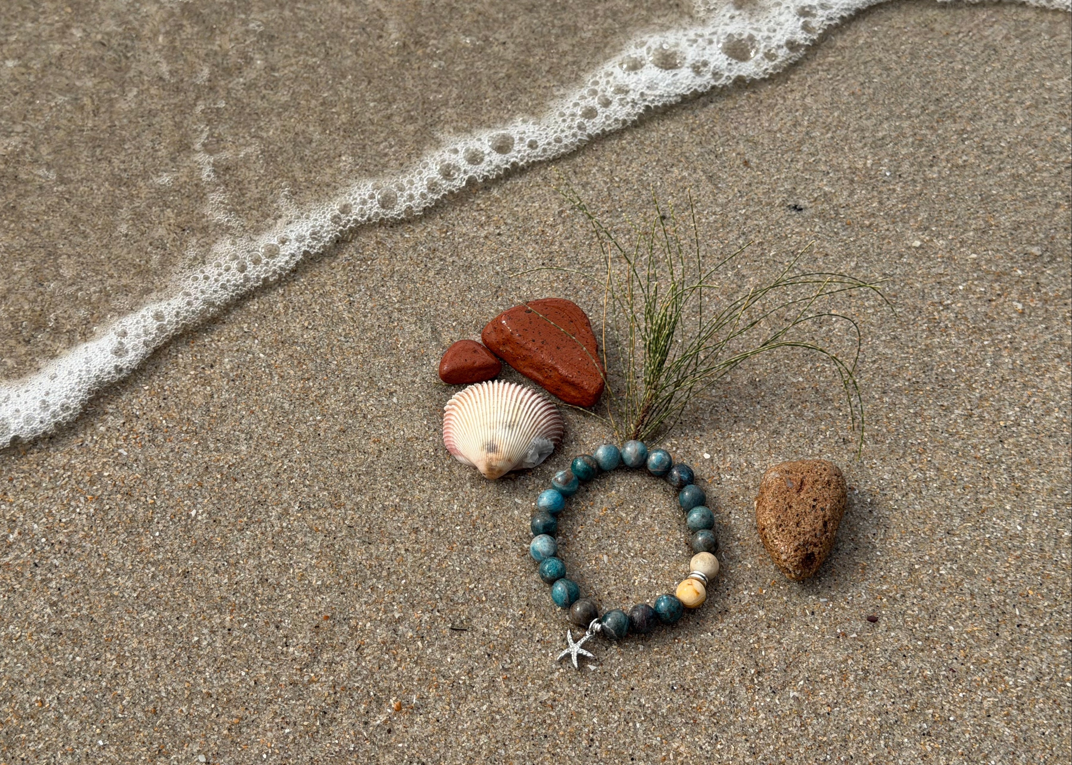 Bracelet with stones and a starfish on sand with ocean waves