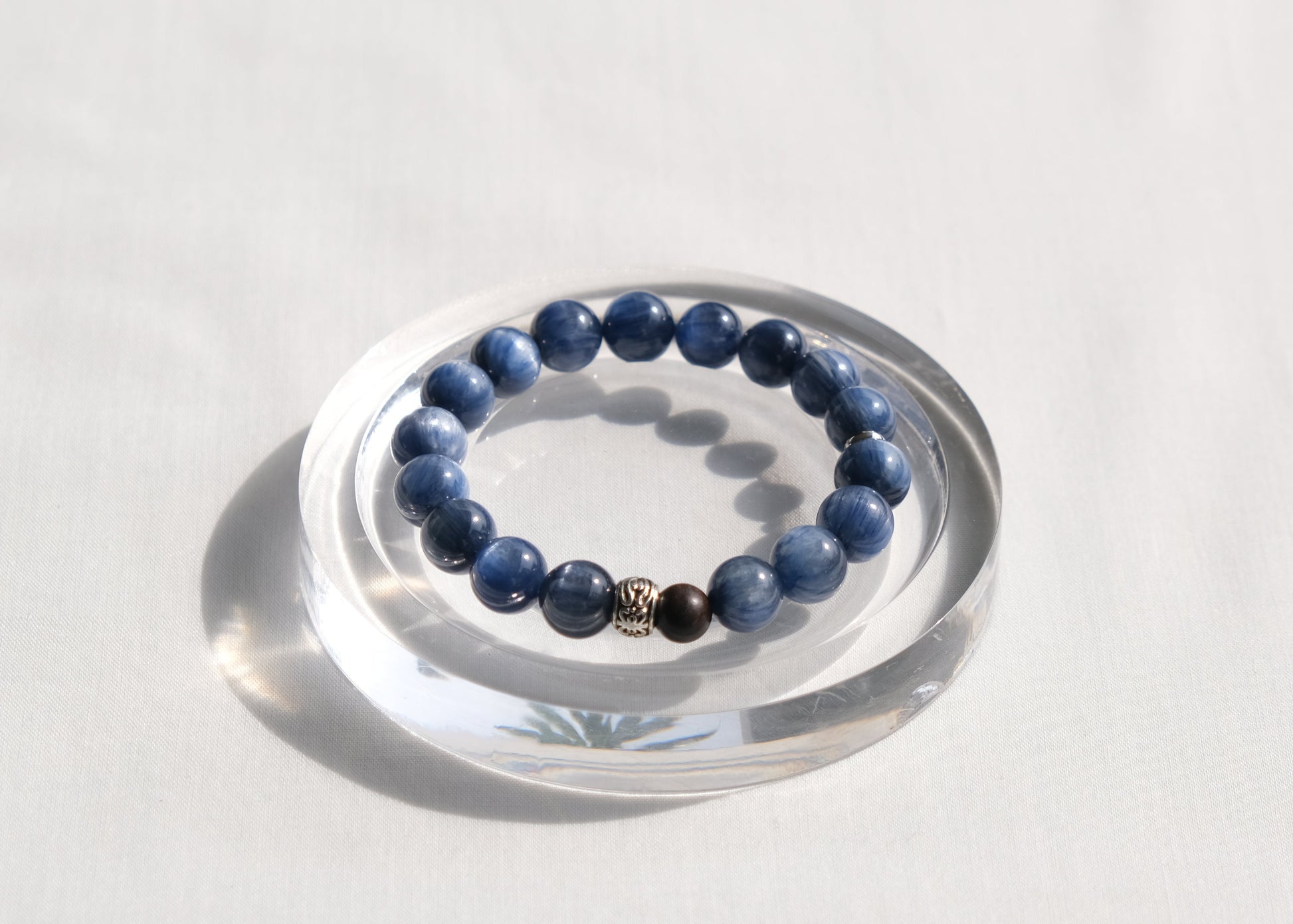 Blue beaded bracelet on a clear circular stand against a white background