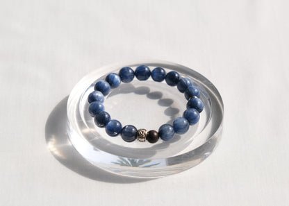 Blue beaded bracelet on a clear circular stand against a white background