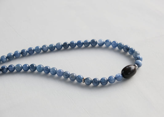 Blue beaded necklace with a black bead on a light gray background