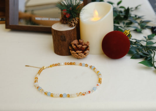 Beaded necklace on a white surface with decorative candles and ornaments.