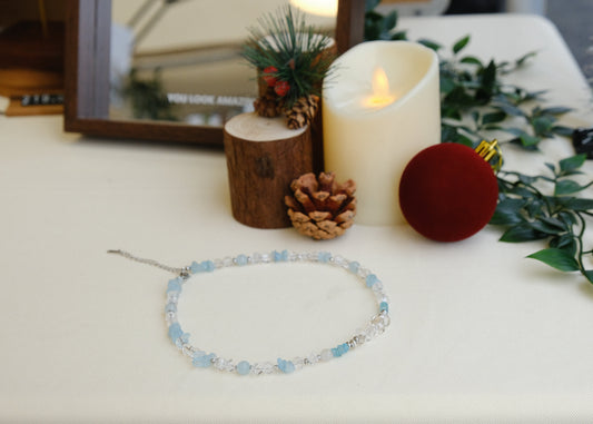Necklace on a white surface with decorative items including a candle and pinecones.