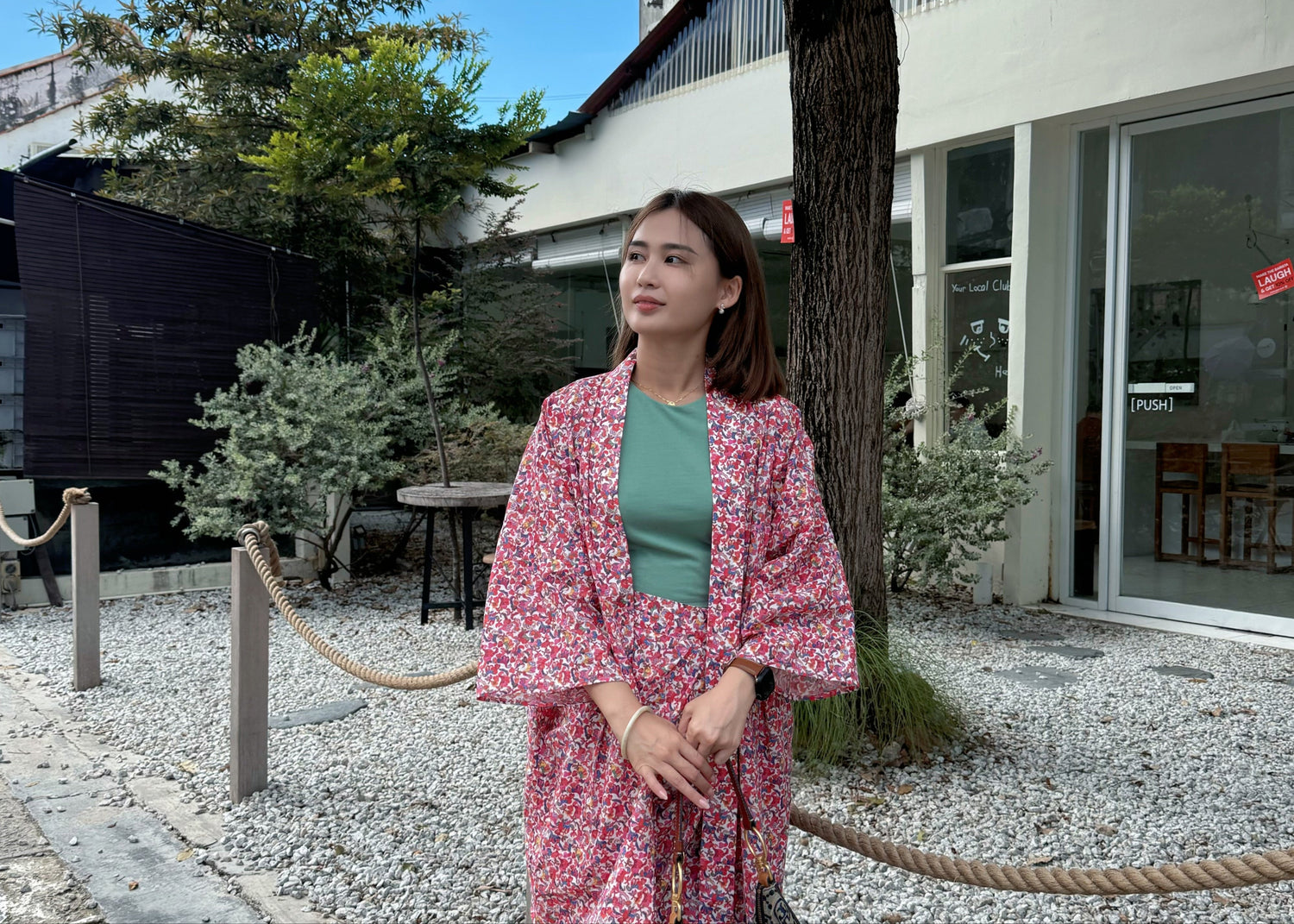 Woman in a pink floral kimono standing on a street with trees and buildings in the background