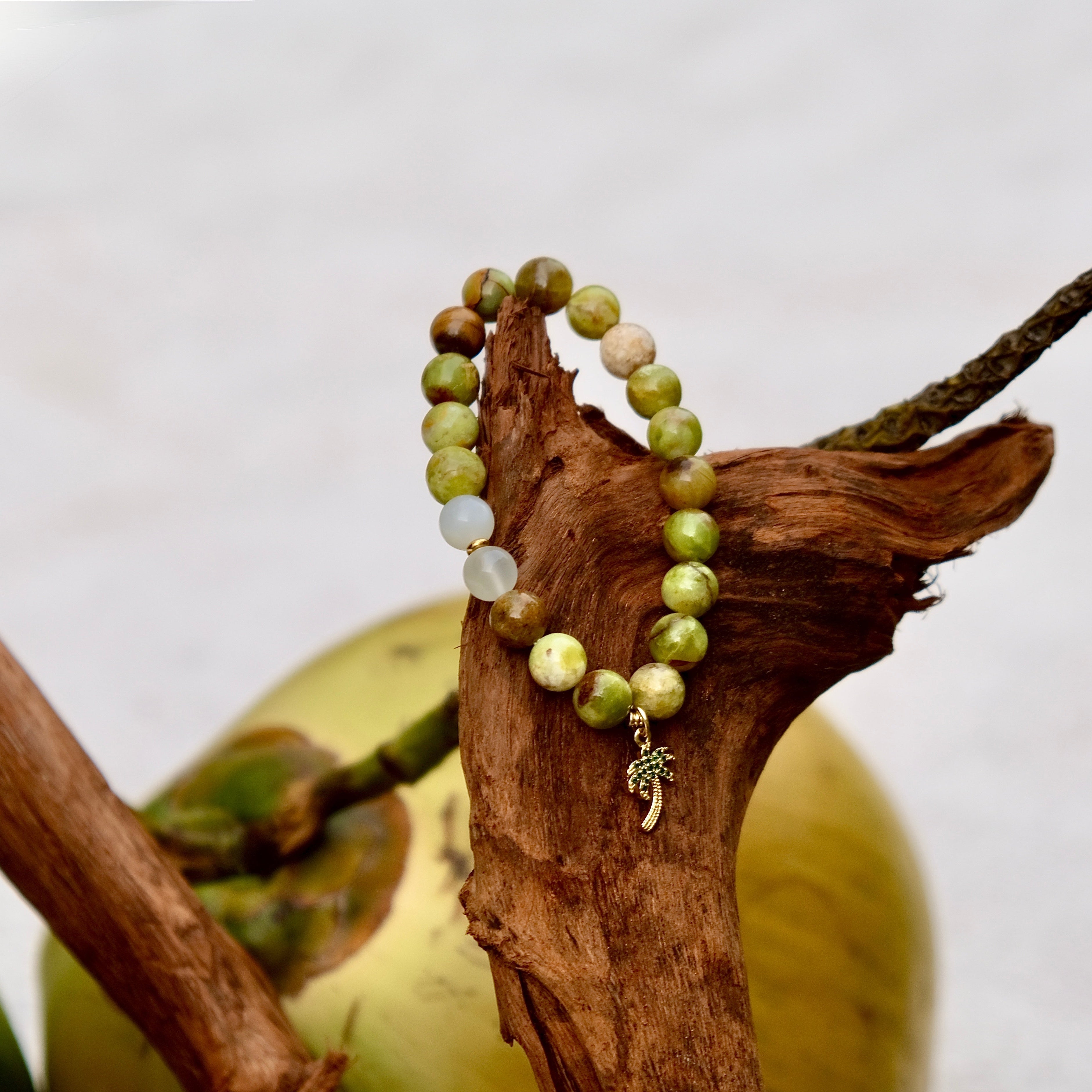 Green beaded bracelet with a charm on a branch with apples in the background