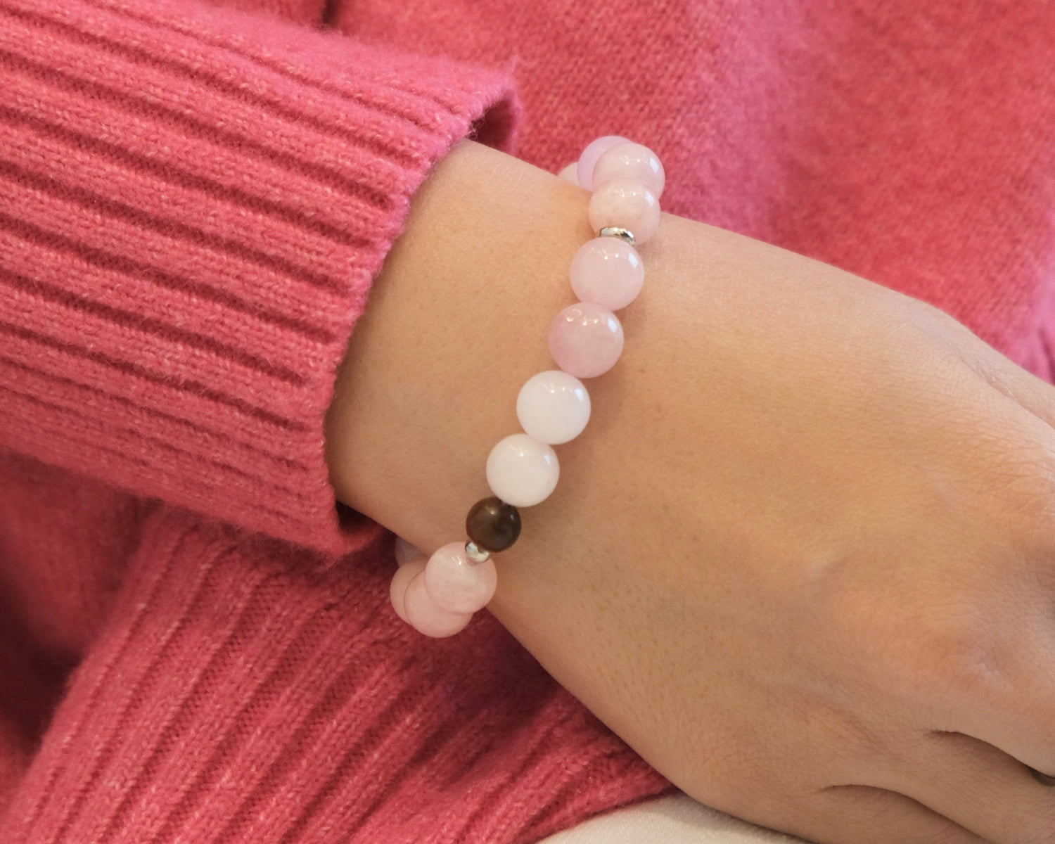 Person wearing a pink sweater and bracelet with a blurred background