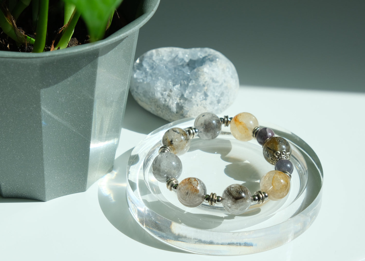 Bracelet with multicolored beads on a clear stand next to a potted plant and stone