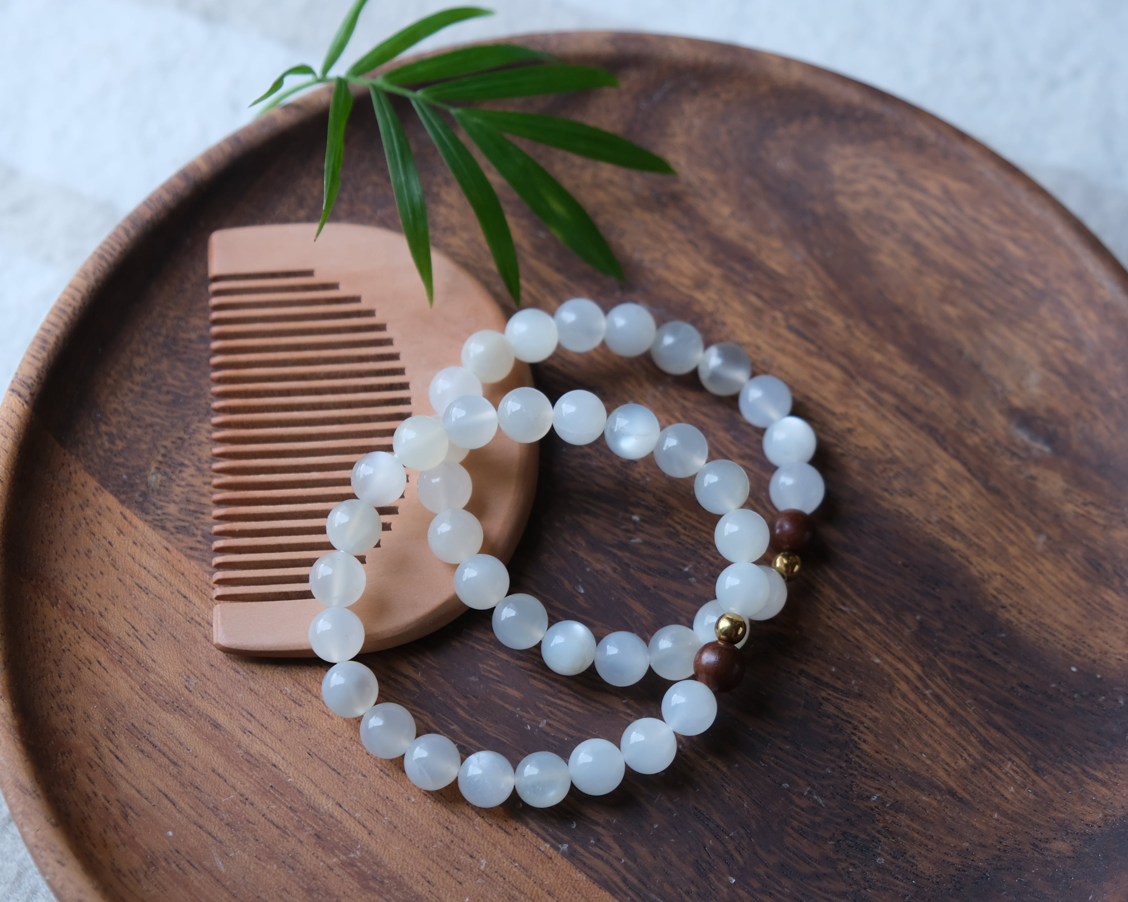 Wooden comb and bracelet on a wooden plate with a leaf on a light background