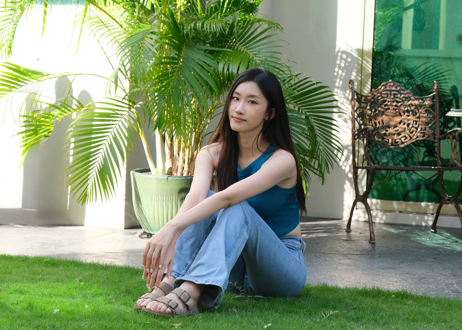 Woman sitting on grass in a garden with plants and a table in the background