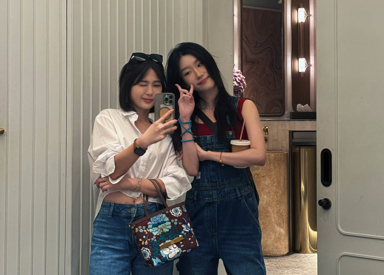 Two women taking a mirror selfie in a room with a door and light fixture.