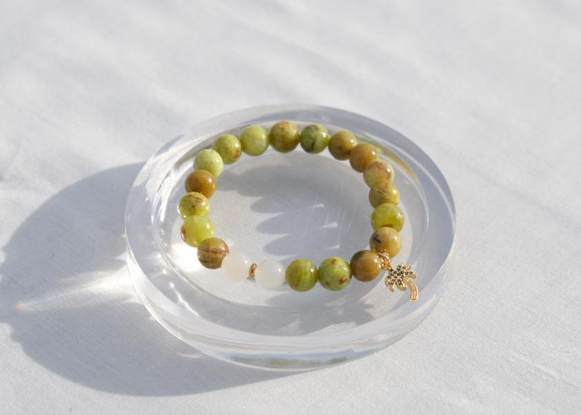 Green beaded bracelet on a clear dish with a white background