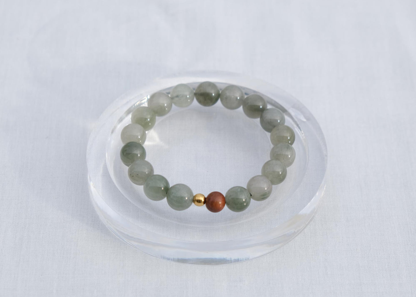 Green beaded bracelet with a gold and red bead on a clear stand against a white background
