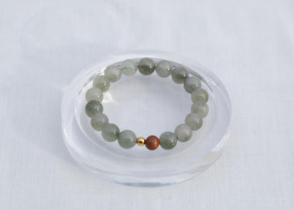 Green beaded bracelet with a gold and red bead on a clear stand against a white background